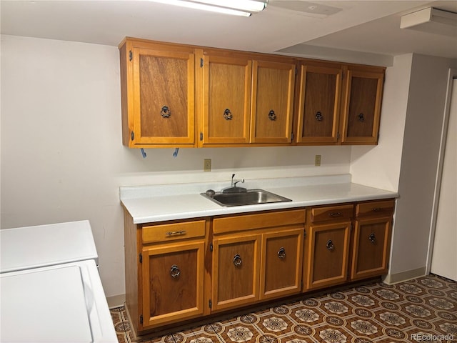 kitchen featuring a sink, dark tile patterned flooring, brown cabinetry, and light countertops