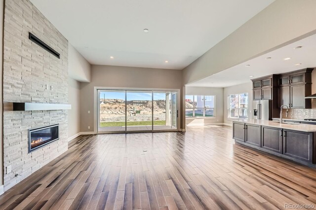 unfurnished living room with a sink, a stone fireplace, wood finished floors, baseboards, and recessed lighting