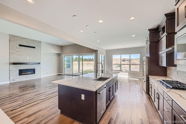 kitchen with a fireplace, stainless steel appliances, light stone countertops, sink, and a kitchen island with sink