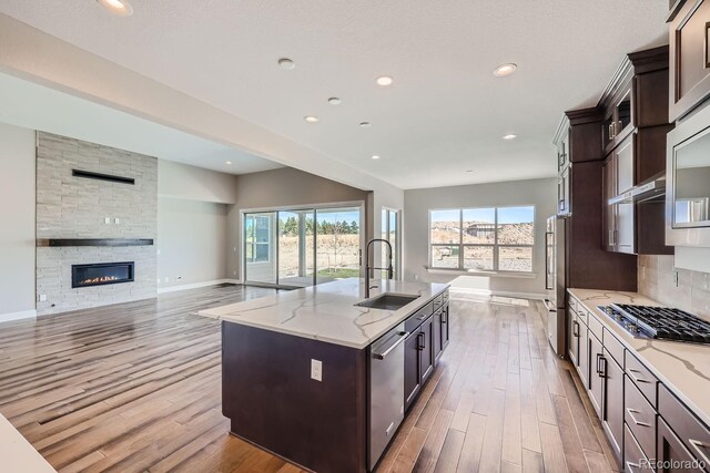 kitchen with a sink, appliances with stainless steel finishes, baseboards, an island with sink, and dark brown cabinets