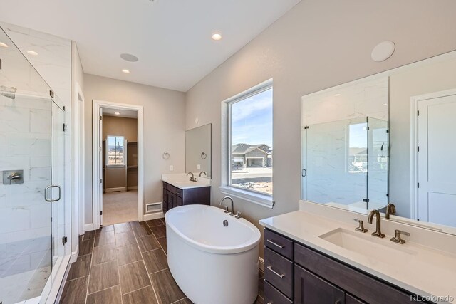 full bath with a stall shower, a soaking tub, two vanities, recessed lighting, and baseboards