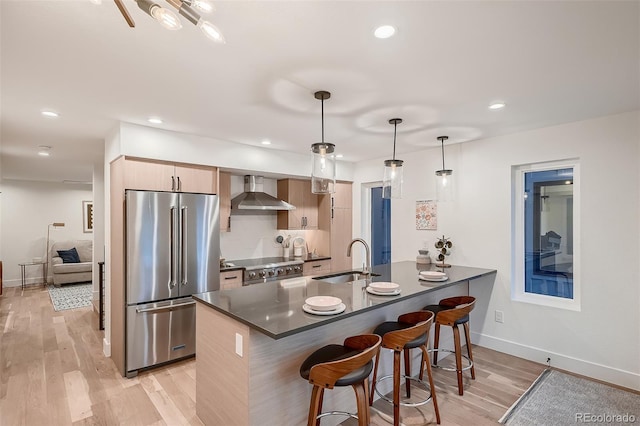 kitchen featuring a breakfast bar, a sink, dark countertops, wall chimney range hood, and high end appliances