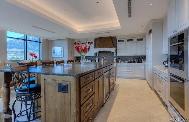 1077 Canyon Blvd Unit 403, Boulder, CO 80302 - kitchen featuring premium range hood, tasteful backsplash, a kitchen breakfast bar, a large island, and white cabinets