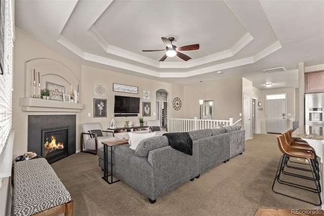 carpeted living room with arched walkways, a raised ceiling, visible vents, a tiled fireplace, and ornamental molding