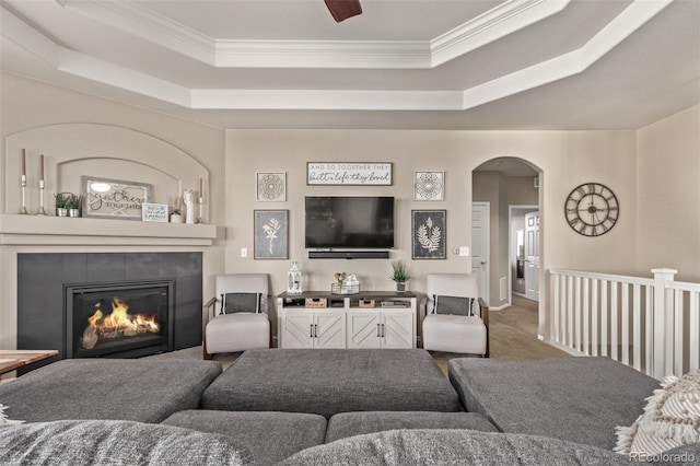 carpeted living area featuring ornamental molding, arched walkways, a raised ceiling, and a tile fireplace