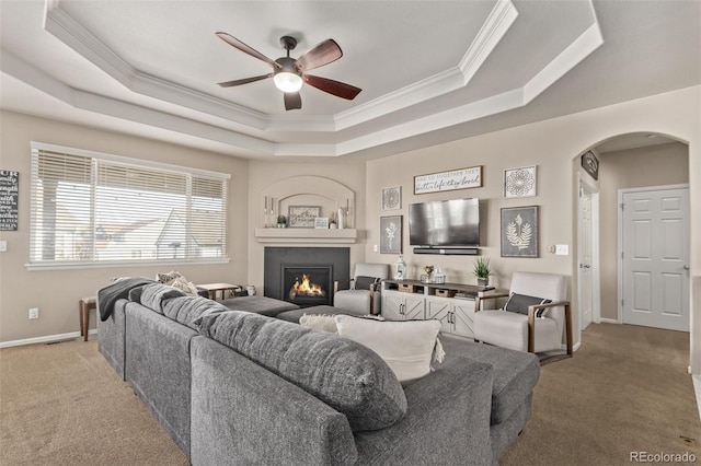 living room featuring carpet floors, a warm lit fireplace, arched walkways, and a tray ceiling