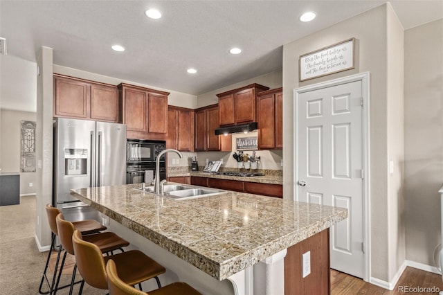 kitchen with under cabinet range hood, a breakfast bar, a sink, light countertops, and black appliances