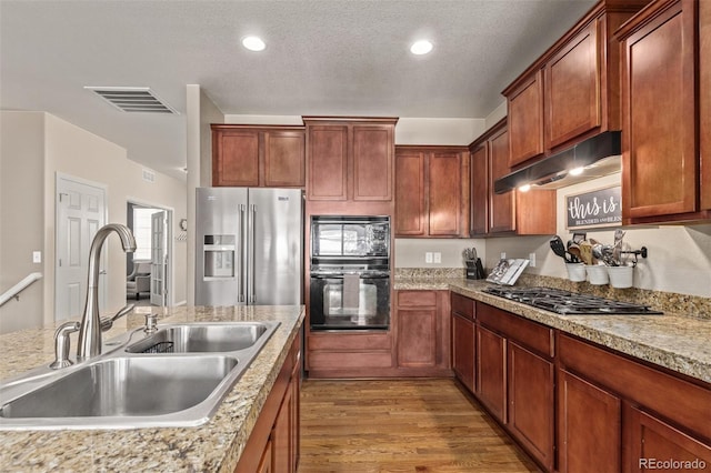 kitchen with light wood-style flooring, under cabinet range hood, a sink, visible vents, and black appliances