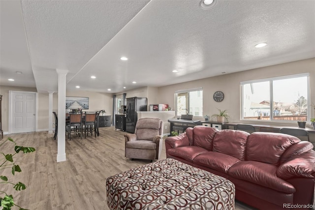 living area featuring ornate columns, light wood-style flooring, a textured ceiling, and recessed lighting