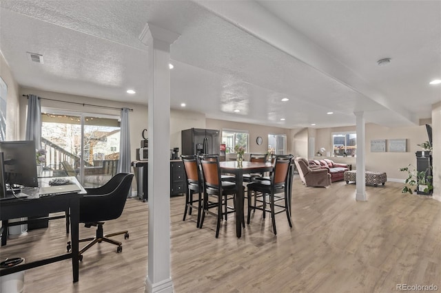 dining room featuring light wood-style floors, decorative columns, baseboards, and a textured ceiling