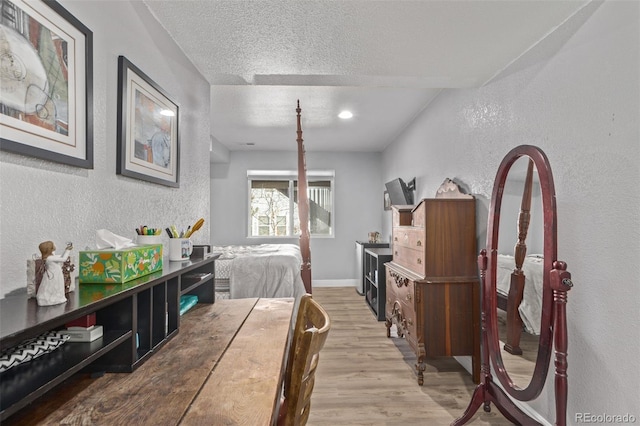 bedroom featuring a textured ceiling, baseboards, wood finished floors, and a textured wall