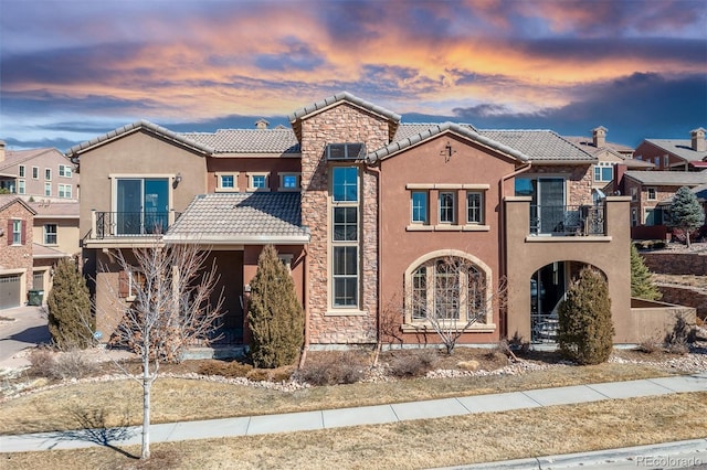 view of front of home with a balcony, stone siding, a tile roof, and stucco siding