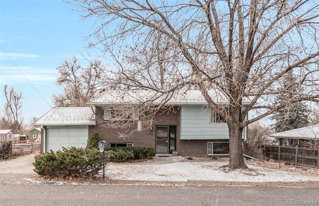 raised ranch with an attached garage, driveway, fence, and brick siding