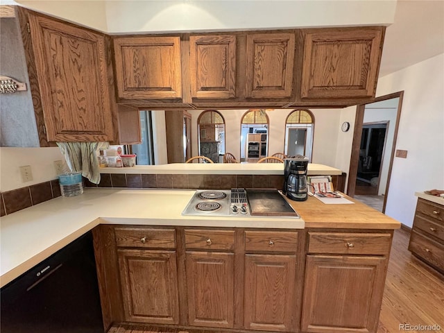 kitchen featuring kitchen peninsula, stainless steel stovetop, light hardwood / wood-style flooring, and black dishwasher