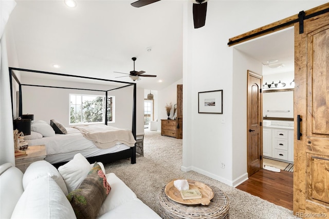 bedroom featuring ceiling fan, ensuite bath, a barn door, and carpet flooring