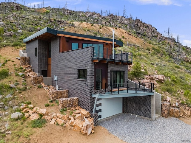 back of property featuring a balcony, gravel driveway, and brick siding