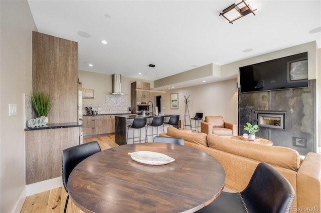 dining room with baseboards, light wood-type flooring, a fireplace, and recessed lighting