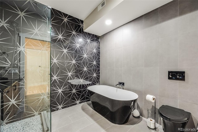 bathroom featuring a freestanding tub, tile patterned flooring, visible vents, and tile walls