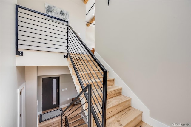 stairway with a high ceiling, baseboards, and wood finished floors