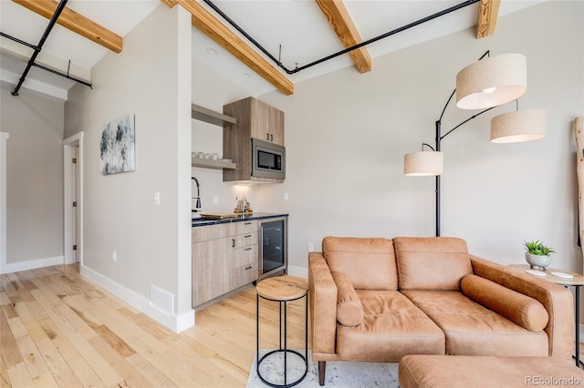 living room featuring beverage cooler, visible vents, light wood finished floors, and beam ceiling