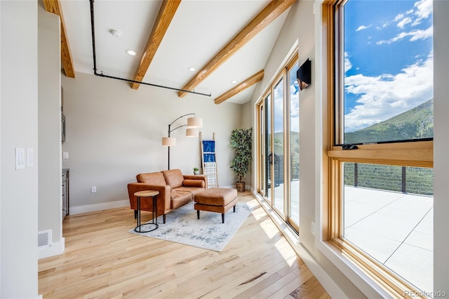 living area with visible vents, beamed ceiling, baseboards, and wood finished floors