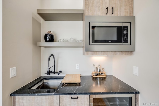 kitchen with dark countertops, beverage cooler, stainless steel microwave, and a sink