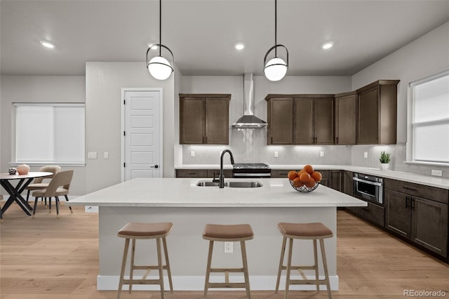 16605 Peak St, Broomfield, CO 80023 - kitchen featuring wall chimney range hood, dark brown cabinetry, backsplash, an island with sink, and a breakfast bar