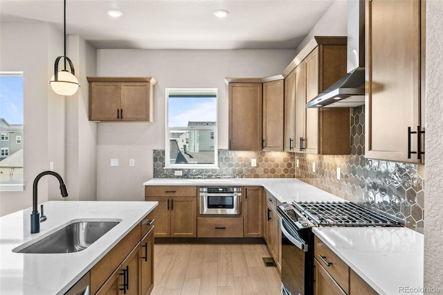 16605 Peak St, Broomfield, CO 80023 - kitchen featuring wall chimney range hood, appliances with stainless steel finishes, light wood finished floors, pendant lighting, and tasteful backsplash