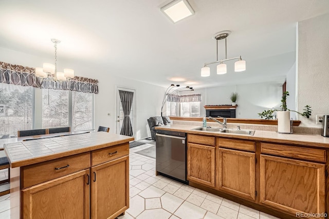 kitchen with tile counters, dishwasher, hanging light fixtures, and sink