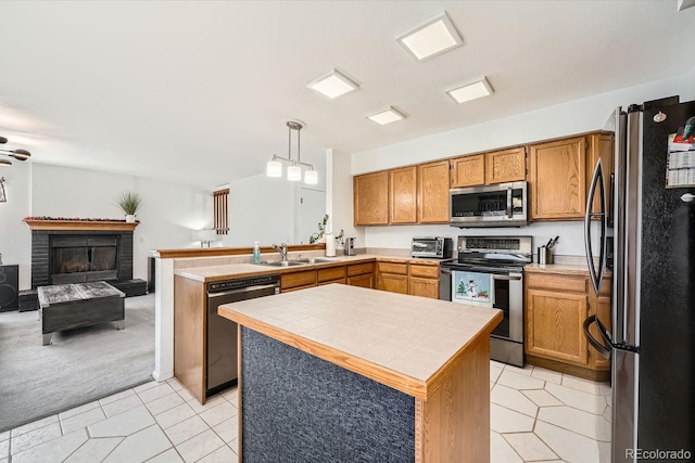 kitchen with hanging light fixtures, a fireplace, appliances with stainless steel finishes, tile counters, and kitchen peninsula