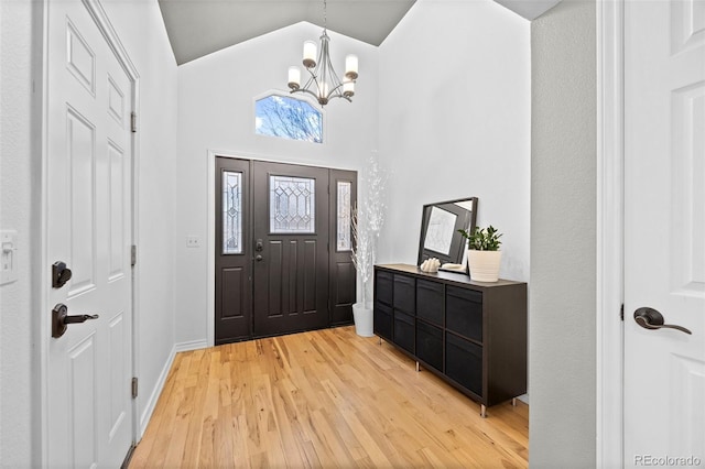 foyer entrance with high vaulted ceiling, light wood-type flooring, and a chandelier