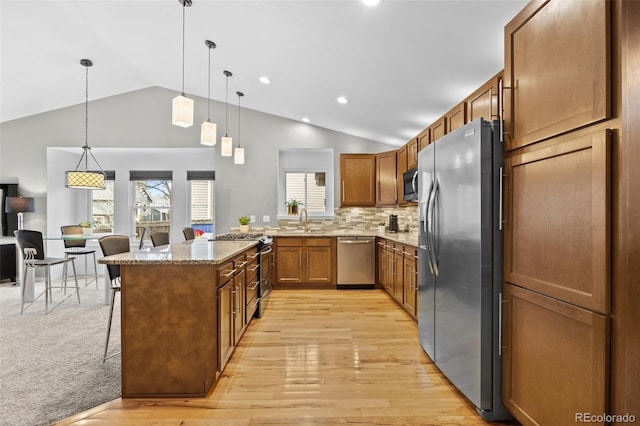 kitchen with appliances with stainless steel finishes, a kitchen breakfast bar, light stone countertops, pendant lighting, and light wood-type flooring