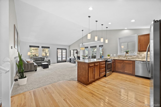 kitchen featuring stainless steel appliances, light stone counters, lofted ceiling, pendant lighting, and kitchen peninsula