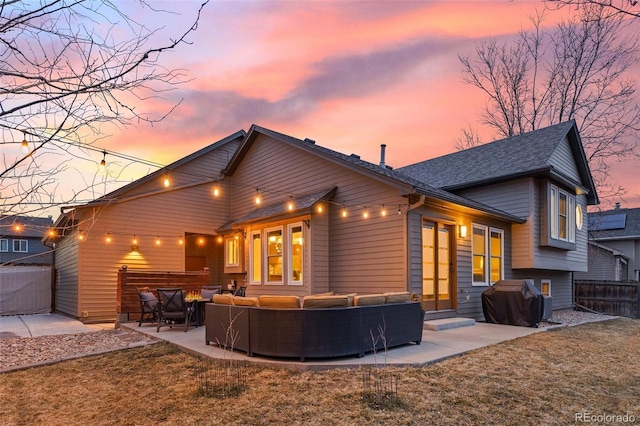 back house at dusk featuring a patio, an outdoor hangout area, and a lawn