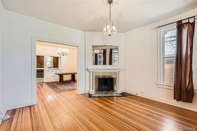 2122 E 13th Ave, Denver, CO 80206 - unfurnished living room featuring light wood finished floors, a tiled fireplace, baseboards, and a chandelier