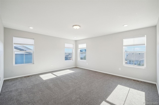 empty room with dark colored carpet and a wealth of natural light