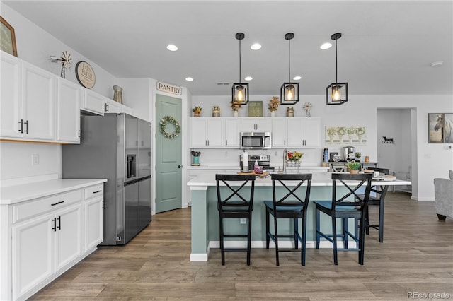 kitchen featuring hanging light fixtures, appliances with stainless steel finishes, white cabinetry, and a kitchen island with sink