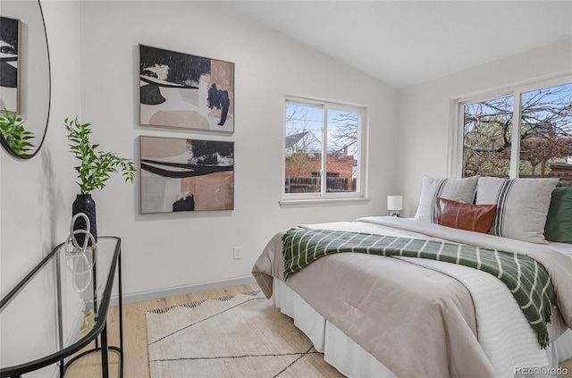 bedroom with light wood finished floors, baseboards, multiple windows, and vaulted ceiling