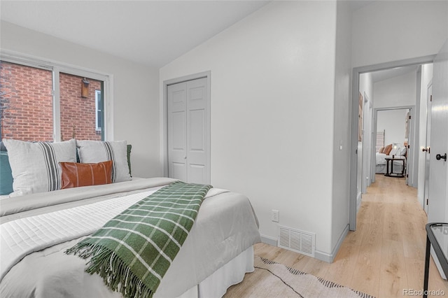 bedroom featuring a closet, baseboards, visible vents, lofted ceiling, and light wood finished floors