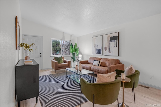 living room featuring light wood-style flooring, a textured ceiling, visible vents, and vaulted ceiling