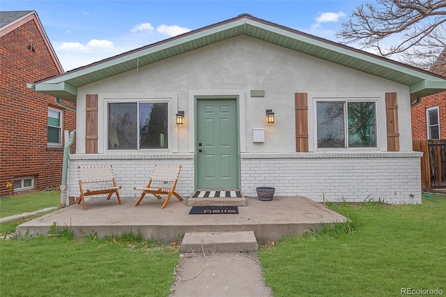 bungalow with a front yard, fence, brick siding, and stucco siding