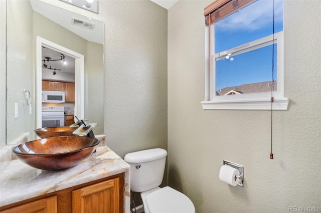 bathroom with vanity, toilet, and rail lighting