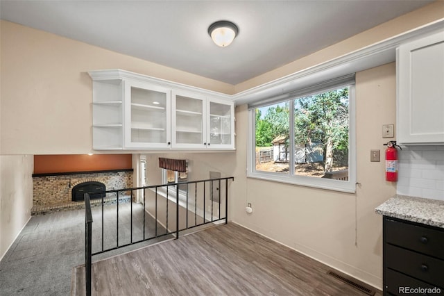 kitchen featuring backsplash, white cabinets, light stone countertops, a fireplace, and dark hardwood / wood-style flooring