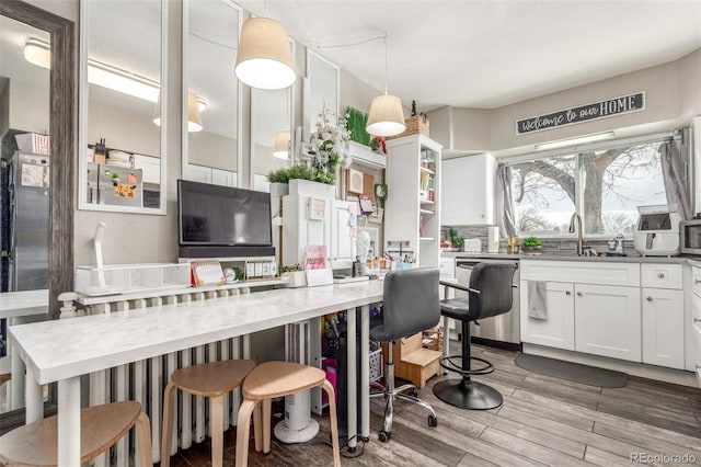 kitchen featuring appliances with stainless steel finishes, pendant lighting, white cabinetry, wood-type flooring, and sink