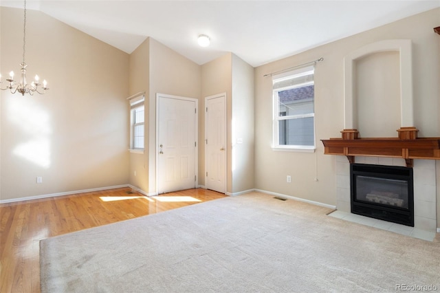 unfurnished living room with an inviting chandelier, light hardwood / wood-style floors, a fireplace, and vaulted ceiling