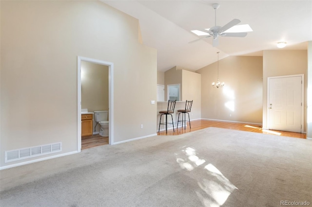 unfurnished living room with ceiling fan with notable chandelier, a skylight, high vaulted ceiling, and light carpet