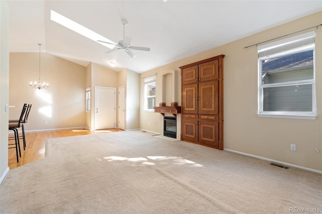 unfurnished living room featuring vaulted ceiling with skylight, ceiling fan with notable chandelier, and light carpet