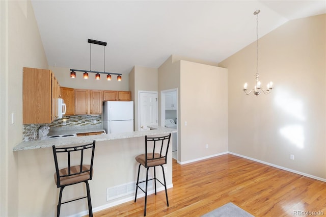 kitchen with kitchen peninsula, white appliances, vaulted ceiling, light hardwood / wood-style flooring, and a kitchen bar