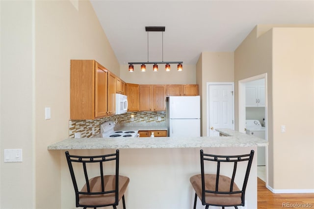 kitchen featuring decorative light fixtures, a kitchen bar, kitchen peninsula, and white appliances