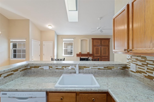 kitchen with ceiling fan, sink, a skylight, white dishwasher, and backsplash